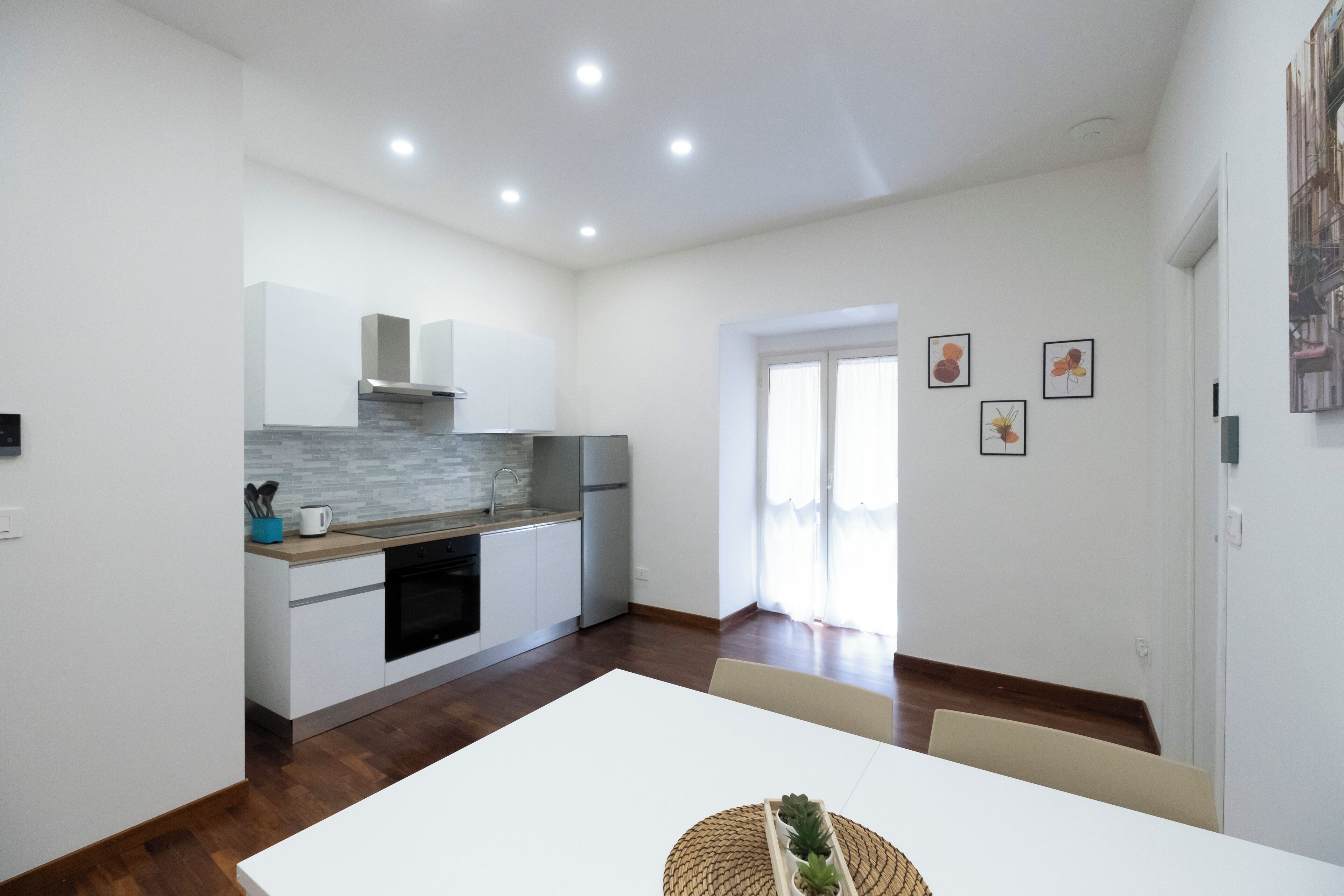 A modern kitchen with white cabinets, a stainless steel range hood, and a wooden countertop. There is a dining table with chairs in the center of the room.