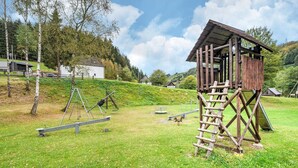 A rustic wooden structure with a ladder, surrounded by a grassy area with playground equipment. - Ferienhaus mit herrlicher Aussicht (Bestwig-Untervalme)