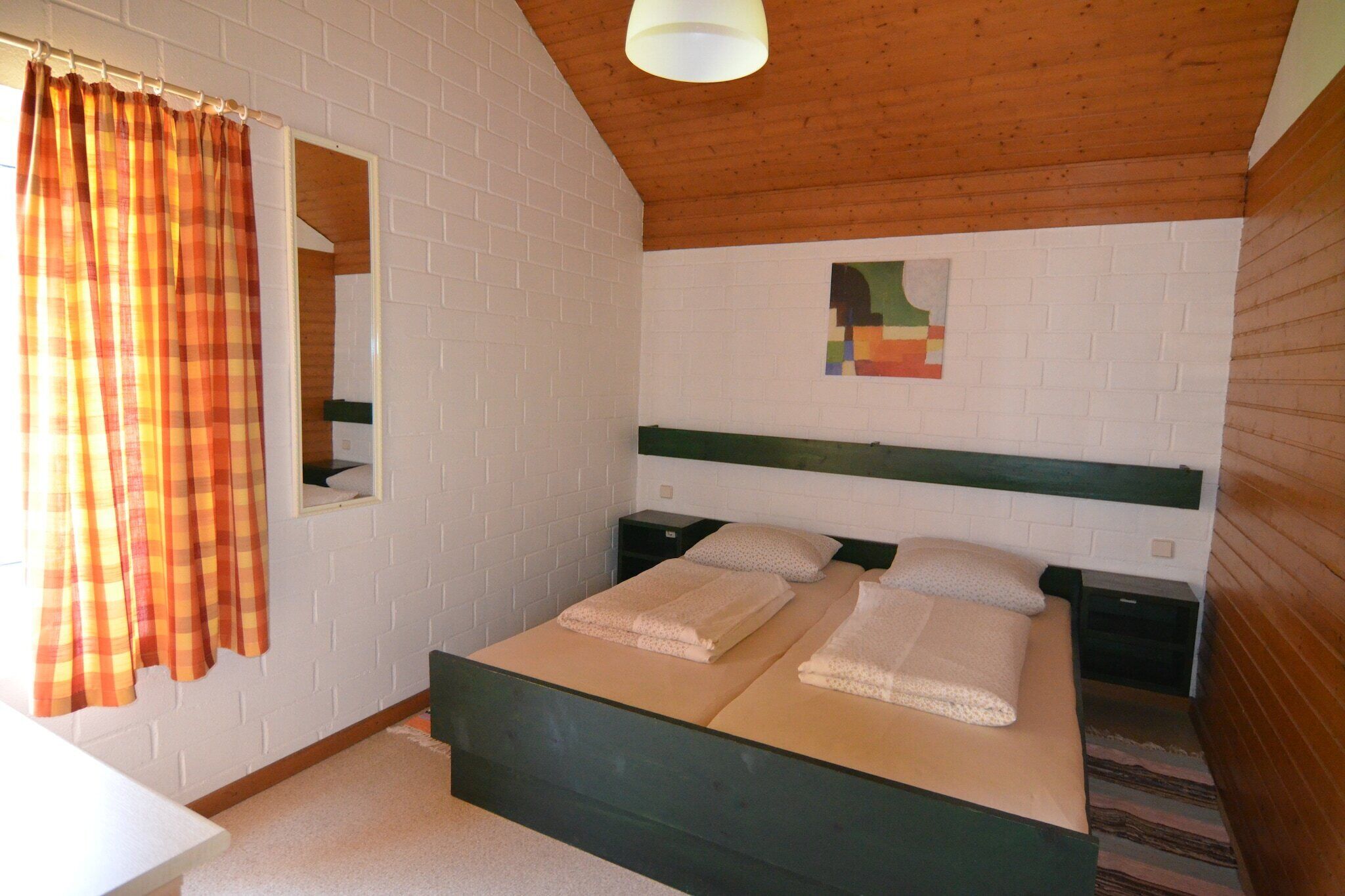A room with a bed, a mirror, a nightstand, and a window with curtains.