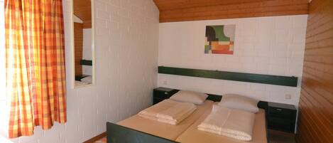 A room with a bed, a mirror, a nightstand, and a window with curtains.