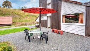 A modern building with a brick exterior and a large window. There is a table and two chairs outside, with a red umbrella providing shade. - Ferienhaus mit herrlicher Aussicht (Bestwig-Untervalme)