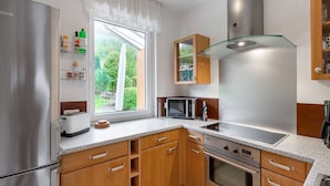 A modern kitchen with wooden cabinets, stainless steel appliances, and a window offering a view of greenery. - Apartment with private terrace in Velmede (Bestwig-Velmede)