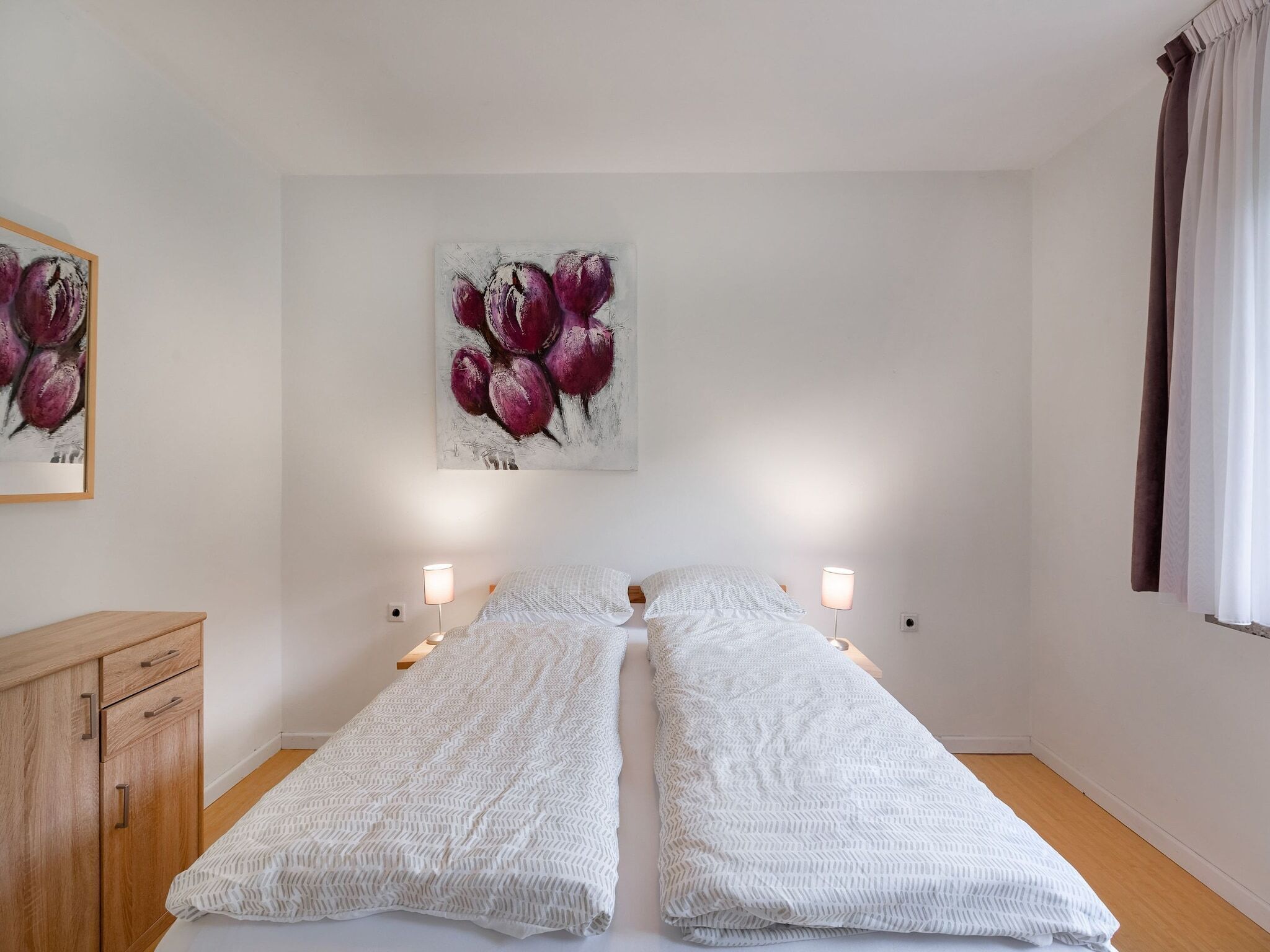 A twin room with two beds, a wooden cabinet, and a painting of purple flowers on the wall.