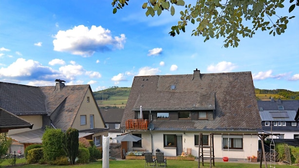 A residential property with a large lawn, a wooden deck, and a two-story house with a sloped roof. - Apartment with private terrace in Velmede (Bestwig-Velmede)