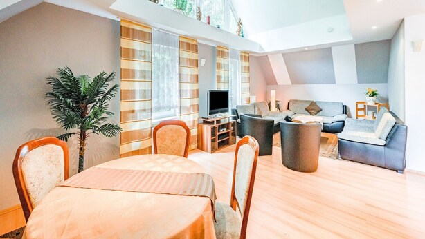 A spacious living room with a high ceiling, a dining area with a table and chairs, and a seating area with sofas and a TV. - Madfeld Apartment Retreat (Brilon-Wald)