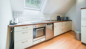 A modern kitchen with white cabinets, a built-in oven, a dishwasher, and a window above the sink. - Madfeld Apartment Retreat (Brilon-Wald)