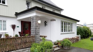 A white house with a red door, stone pillar, and a small porch area with potted plants.