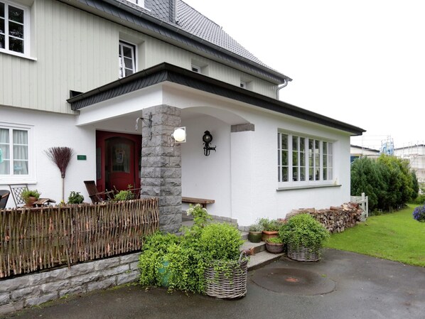 A white house with a red door, stone pillar, and a small porch area with potted plants. - Winterberg Gruppenhaus mit Sauna – ideal für Familien & Freunde (Winterberg)