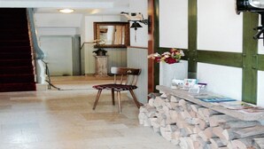 A hallway with a wooden chair, a stack of firewood, a mirror, and a wall-mounted light fixture.