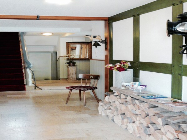 A hallway with a wooden chair, a stack of firewood, a mirror, and a wall-mounted light fixture. - Winterberg Gruppenhaus mit Sauna – ideal für Familien & Freunde (Winterberg)