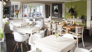 A modern dining area with white furniture, a wooden table, and a view of the street through large windows.