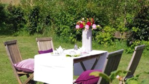 An outdoor dining area with a table set for two, surrounded by chairs with cushions. A vase with flowers is placed on the table. - Winterberg Gruppenhaus mit Sauna – ideal für Familien & Freunde (Winterberg)