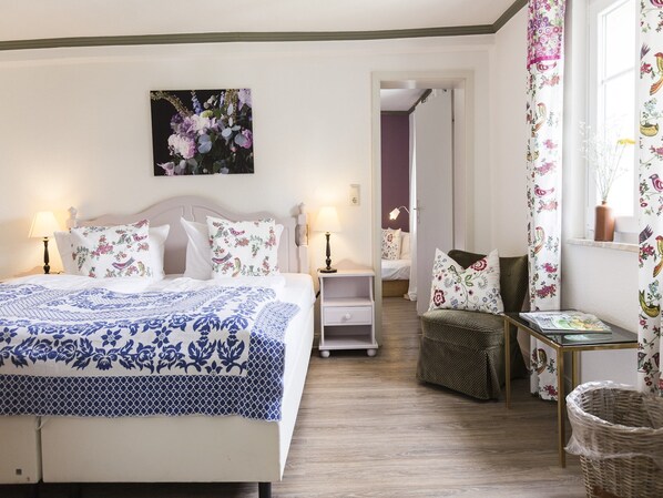A bedroom with a bed, bedside tables, a nightstand, a chair, a small table, a lamp, a picture on the wall, and a window with curtains. - Winterberg Gruppenhaus mit Sauna – ideal für Familien & Freunde (Winterberg)