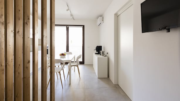 A modern kitchen with white cabinetry, a dining area with a white table and chairs, and a flat-screen TV mounted on the wall. - Visitsicilia Vasile 9 - 2 (Castellammare del Golfo)