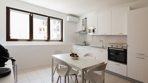 Eine moderne Küche mit weißen Schränken, einem Esstisch mit Stühlen, einer Mikrowelle, einem Backofen und einem Fenster mit Jalousien.