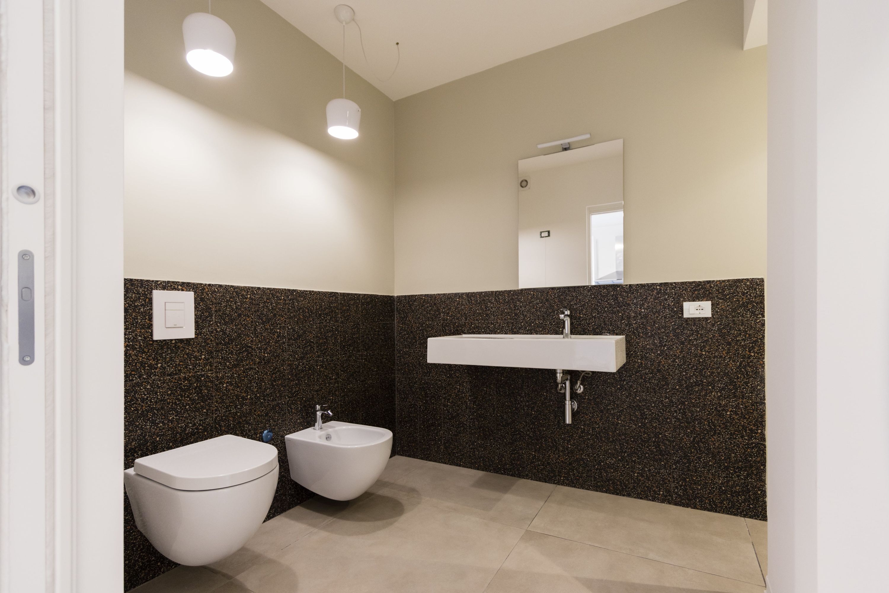 Une salle de bain moderne avec des toilettes, un bidet et un lavabo, le tout adossé à un mur à motifs.