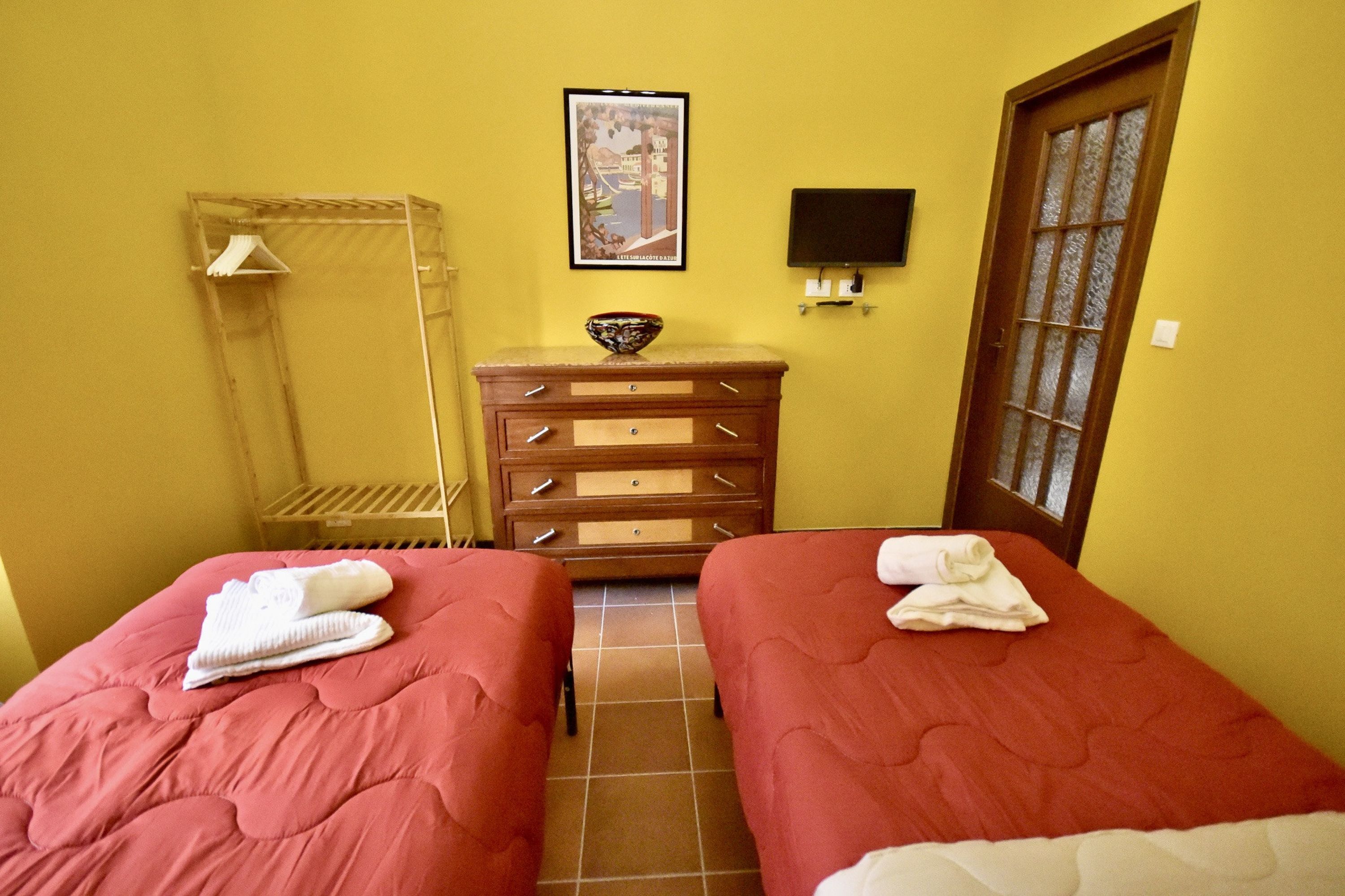 Una habitación con dos camas, un aparador de madera, un cuadro enmarcado en la pared y una puerta con panel de vidrio esmerilado.