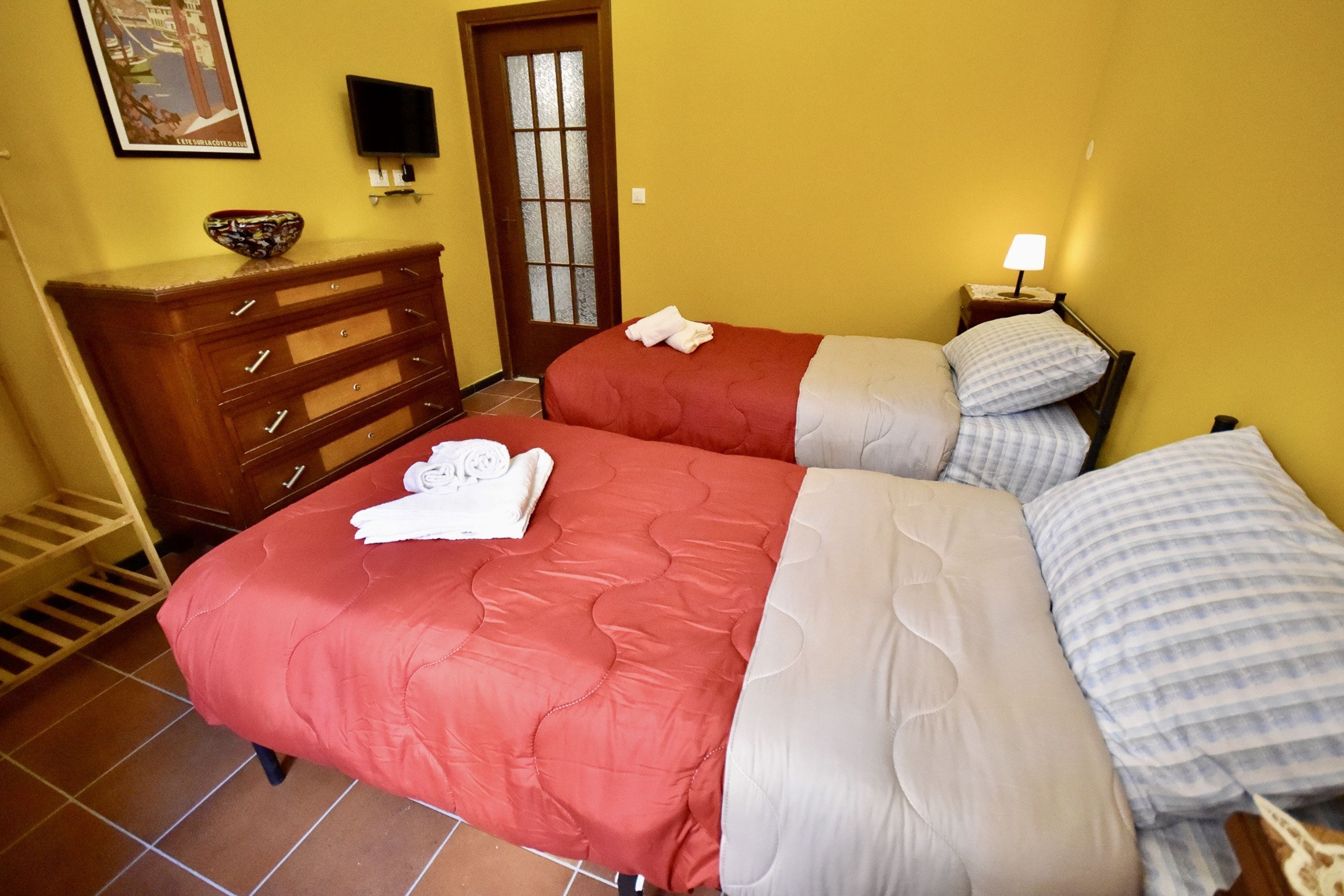 A hotel room with two beds, a wooden dresser, a television, and a door with glass panels.