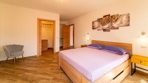 Un dormitorio con una cama, una silla, una mesita de noche de madera y una lámpara de pared.