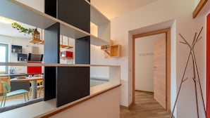 Un interior moderno con una zona de cocina al fondo, suelo de madera y una puerta que da a otra habitación.