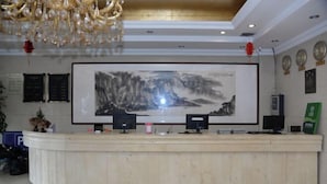 A reception desk with a large framed artwork above it, a chandelier, and a wall with clocks and plaques. - Fubainian Business Hotel (Qingdao)