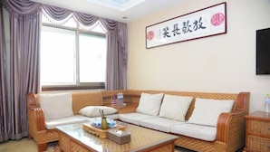 A living room with a sofa, a coffee table, and a television on the wall. - Fubainian Business Hotel (Qingdao)