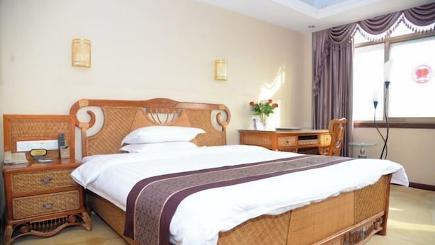 A hotel room with a large bed, a bedside table, a desk, and a chair. - Fubainian Business Hotel (Qingdao)