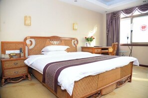 A hotel room with a large bed, a bedside table, a desk, and a chair.