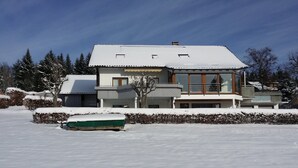 Moderni, kaksikerroksinen talo, jonka katto on lumen peitossa ja jonka etupihalla on vihreä vene.