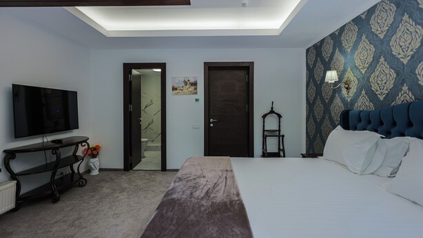 A hotel room with a bed, a TV, a desk, a chair, and a patterned wall. - Villa Tom (Sinaia)