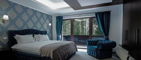 A bedroom with a large bed, a blue upholstered chair, and a view of the outdoors through a sliding glass door.