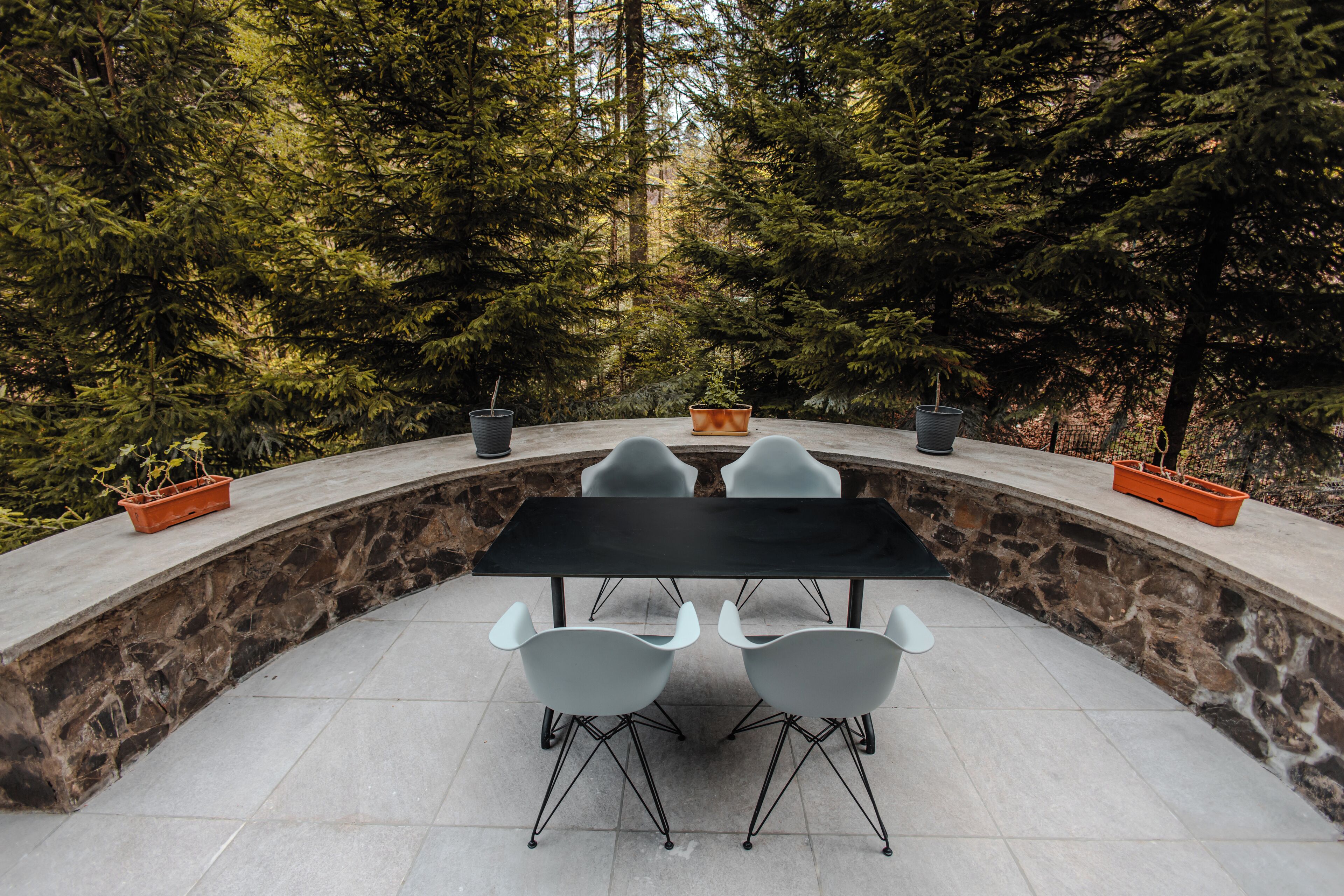 Un espace de restauration en plein air, avec un mur en pierre et une table noire entourée de chaises blanches.