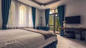 A bedroom with a large bed, a desk, a chair, a coat rack, and a TV.