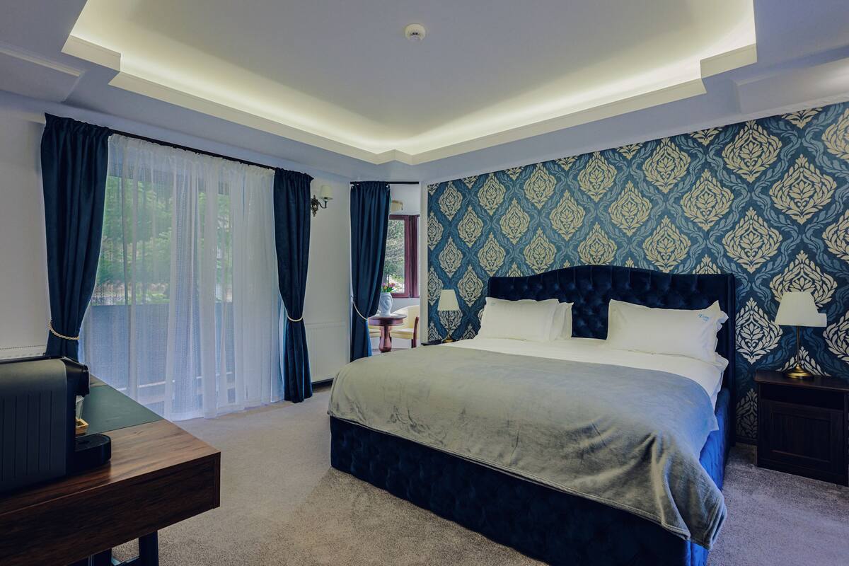 A bedroom with a large bed, a desk, and a window with curtains.