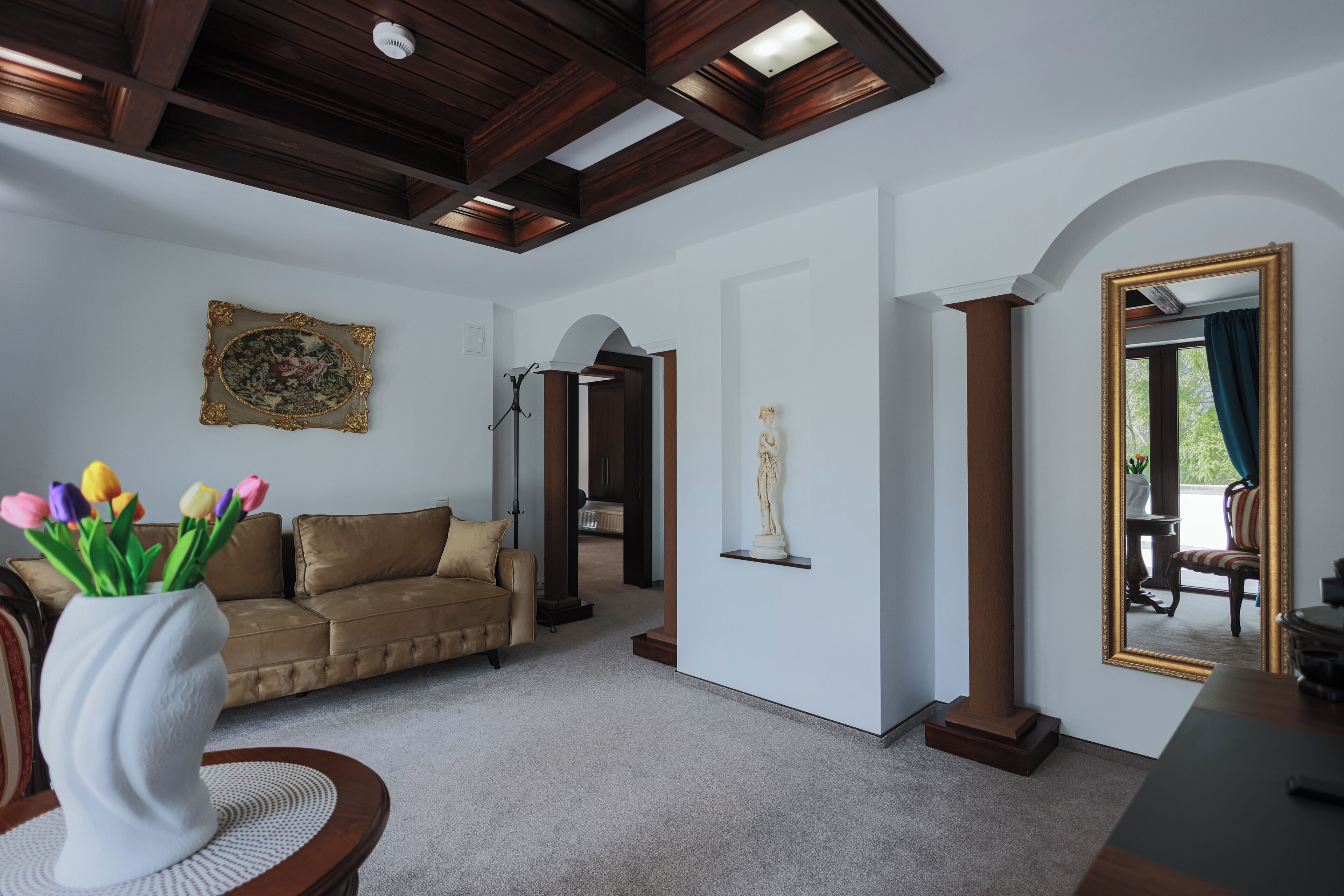 A living room with a brown sofa, a white vase with tulips, a framed picture, and a mirror with a gold frame.