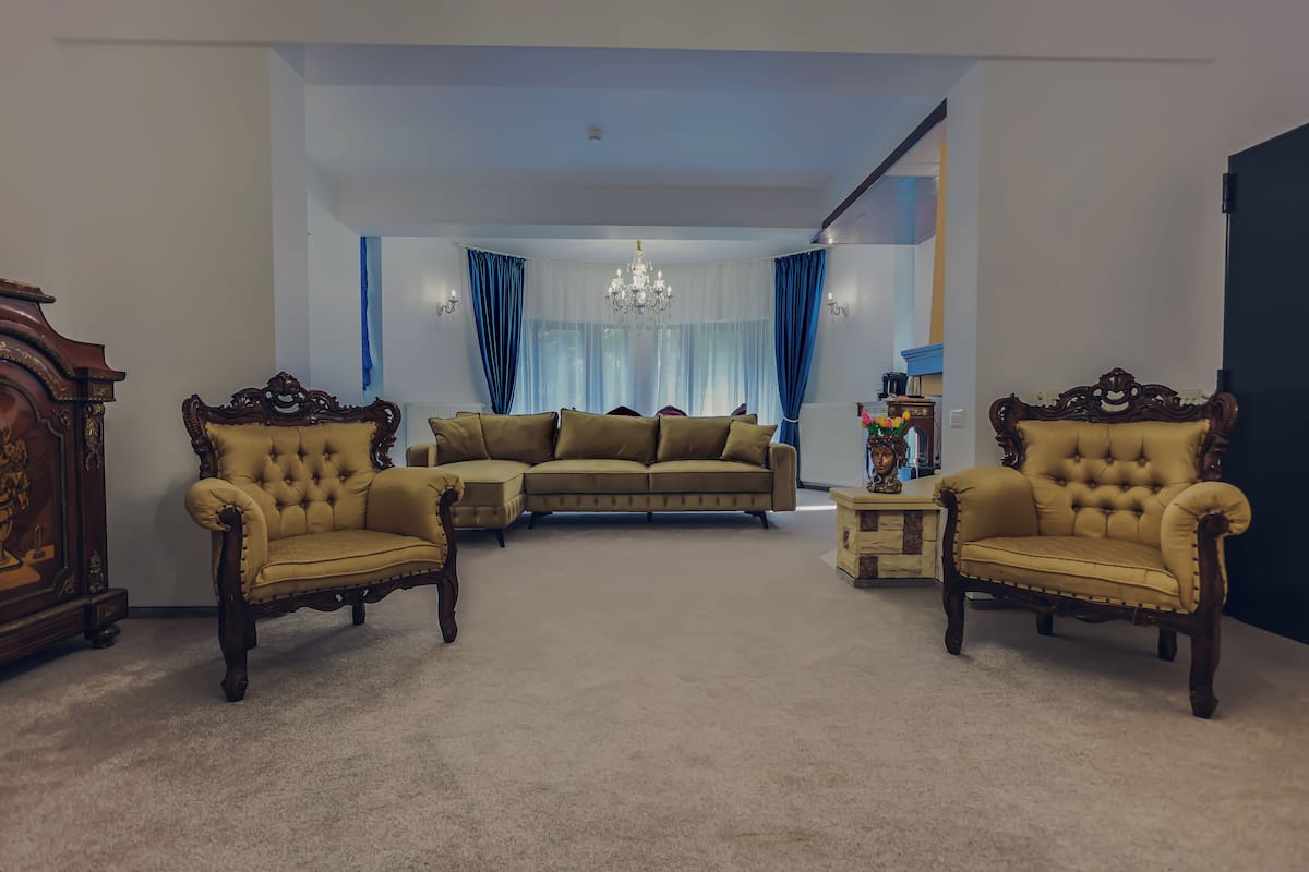 A living room with a beige sectional sofa, two ornate armchairs, a small side table, and a chandelier.
