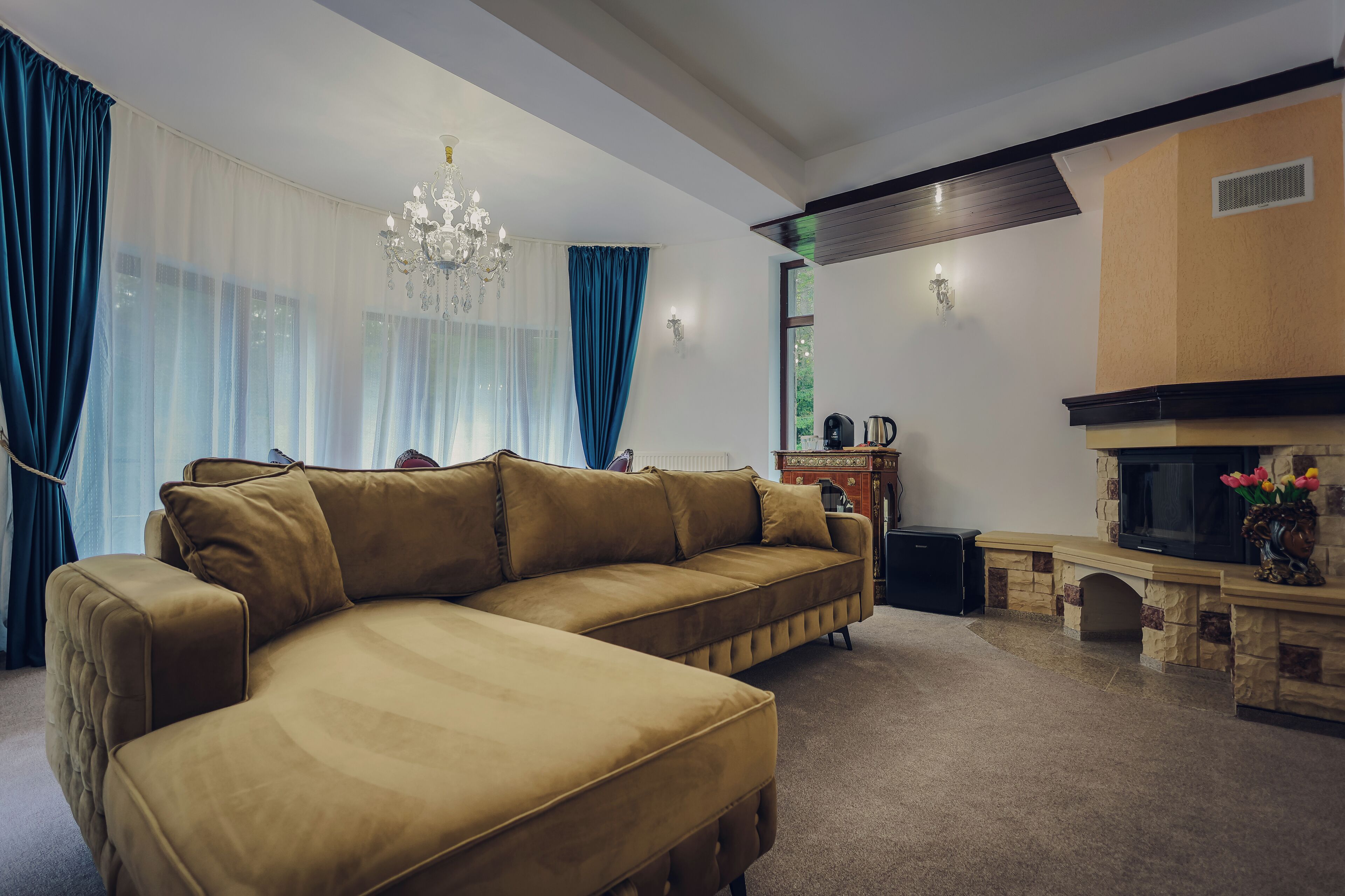 A living room with a large sectional sofa, a chandelier, a fireplace, and a stone fireplace surround.