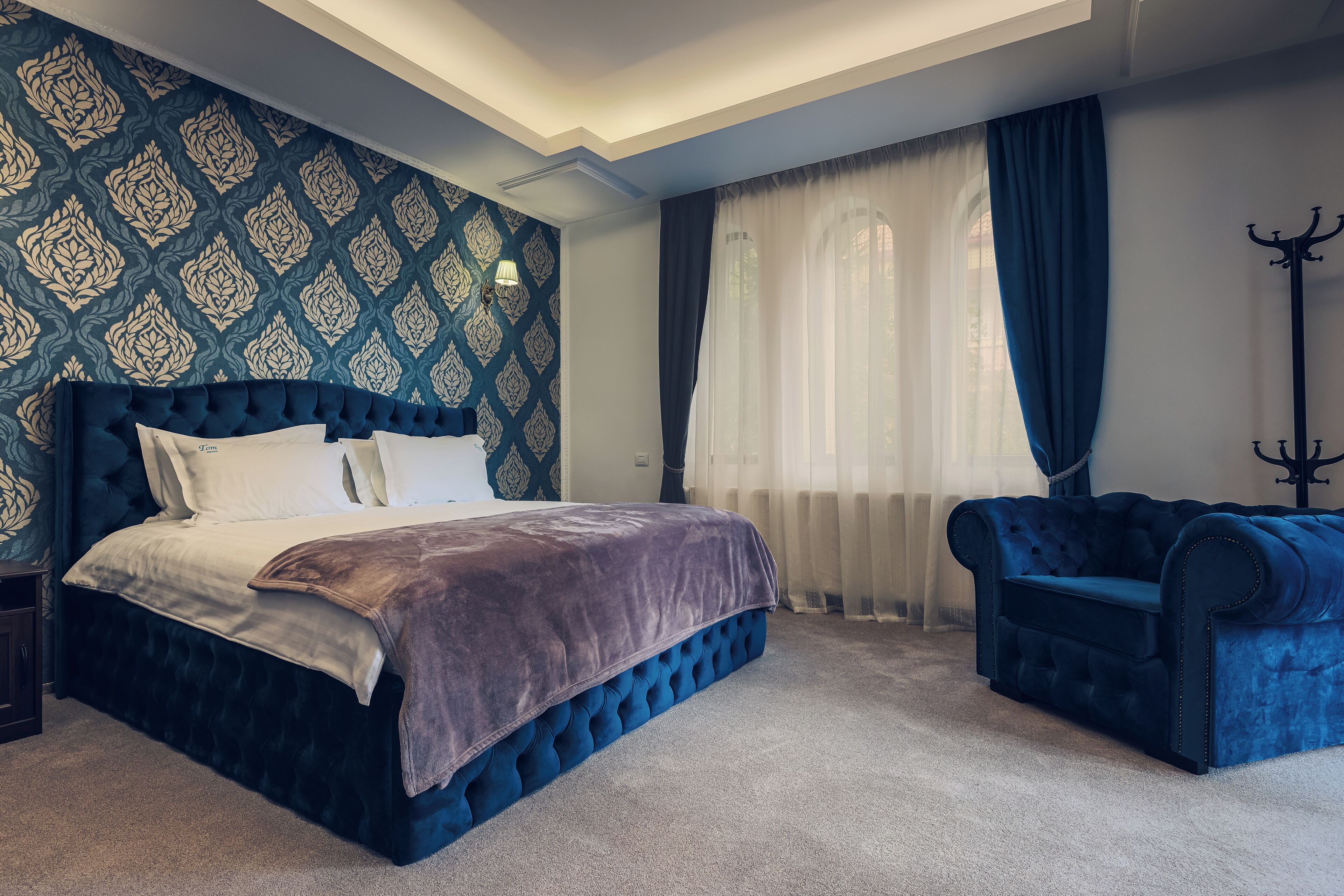A bedroom with a large bed, a blue upholstered sofa, and a patterned wallpaper.