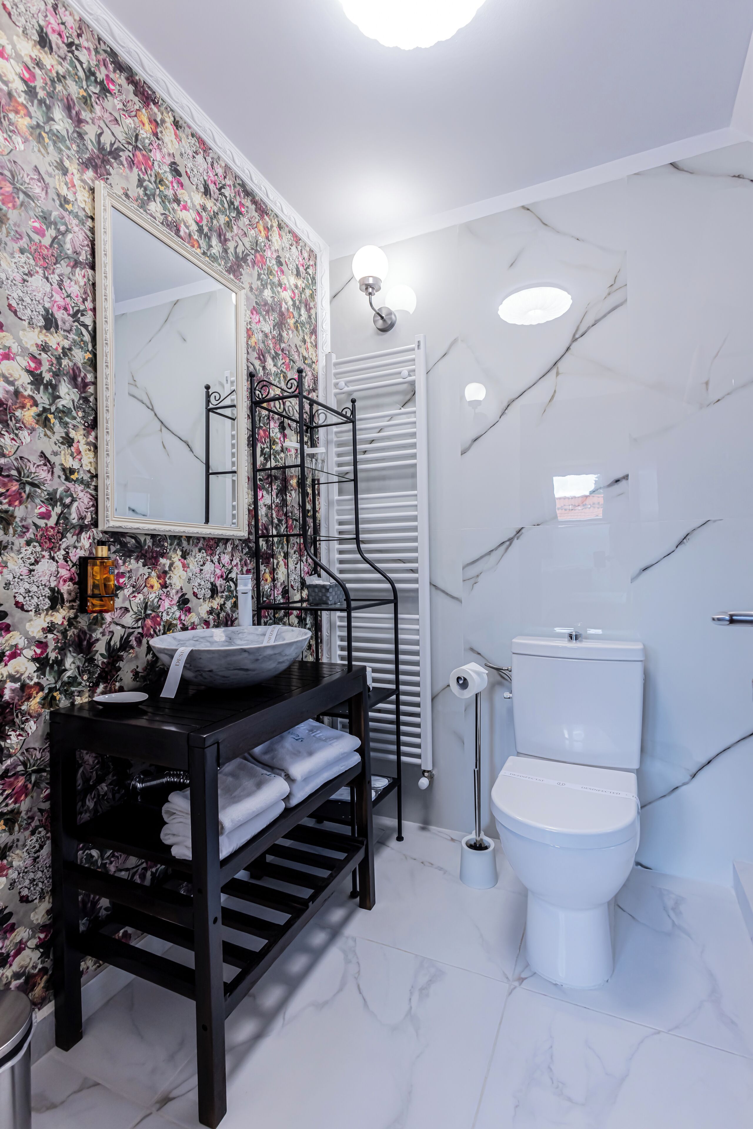 A bathroom with a black vanity, white marble walls, a white toilet, and a floral wallpaper design.