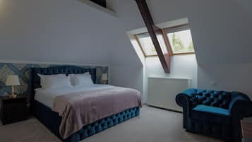 A bedroom with a large bed, a blue upholstered chair, a nightstand, and a window with a view of trees.