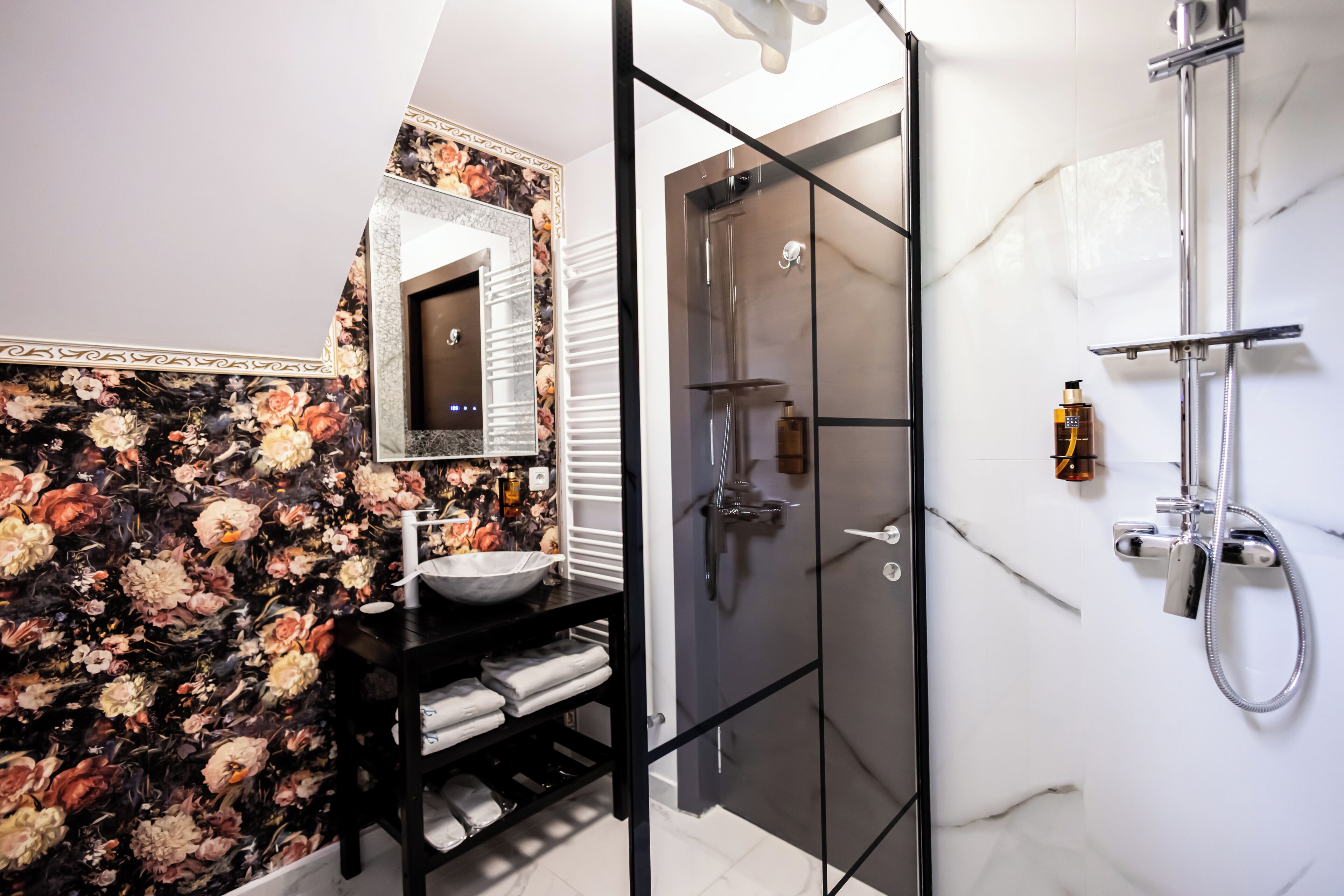 Een moderne badkamer met een douchecabine van glas, een marmeren wand en een behang met bloemenmotief.