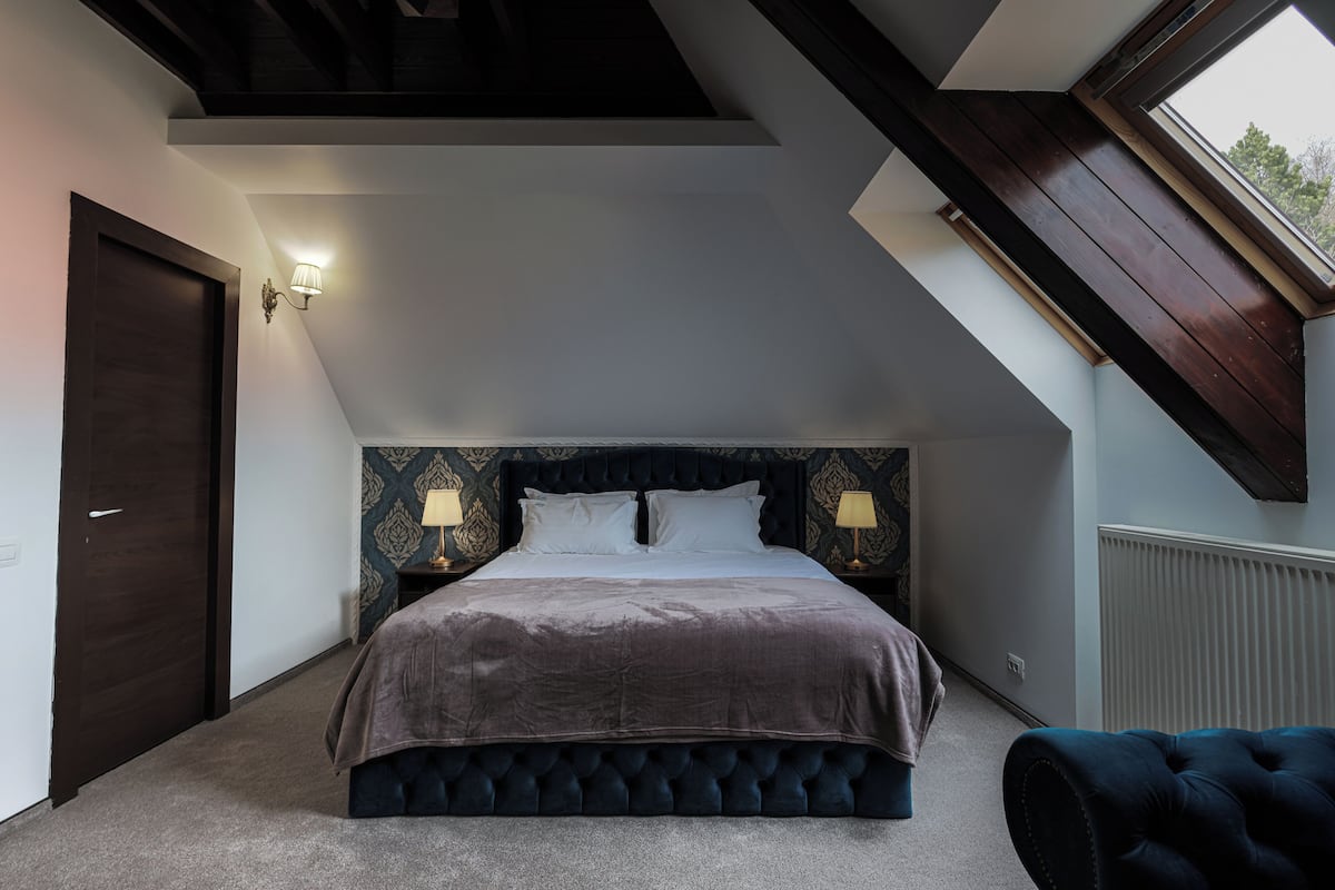 A bedroom with a vaulted ceiling, a large bed with two bedside tables, and a window.