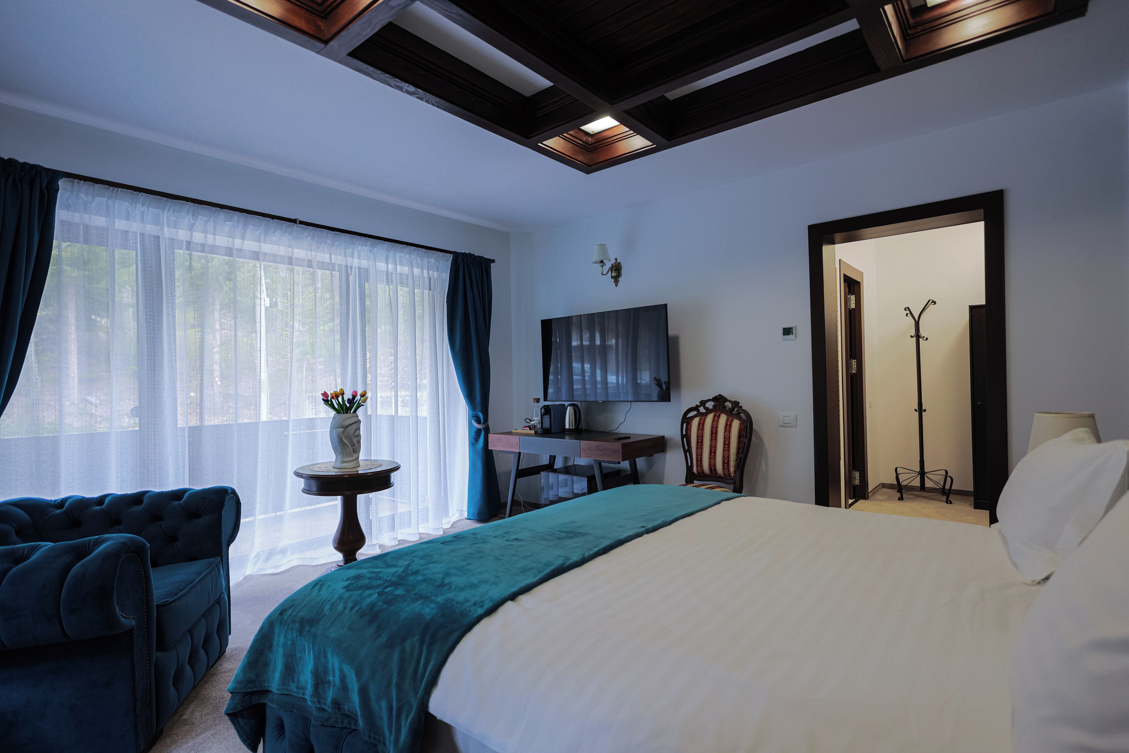 A hotel room with a large bed, a desk, a chair, a TV, and a coat rack.