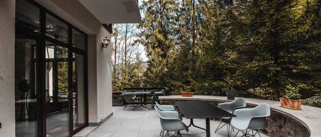 An outdoor patio with a dining table and chairs, surrounded by potted plants and trees.
