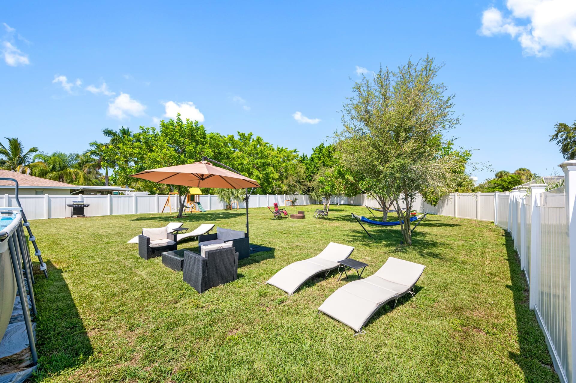 A backyard with a lawn, outdoor furniture, a hammock, and a swing set.