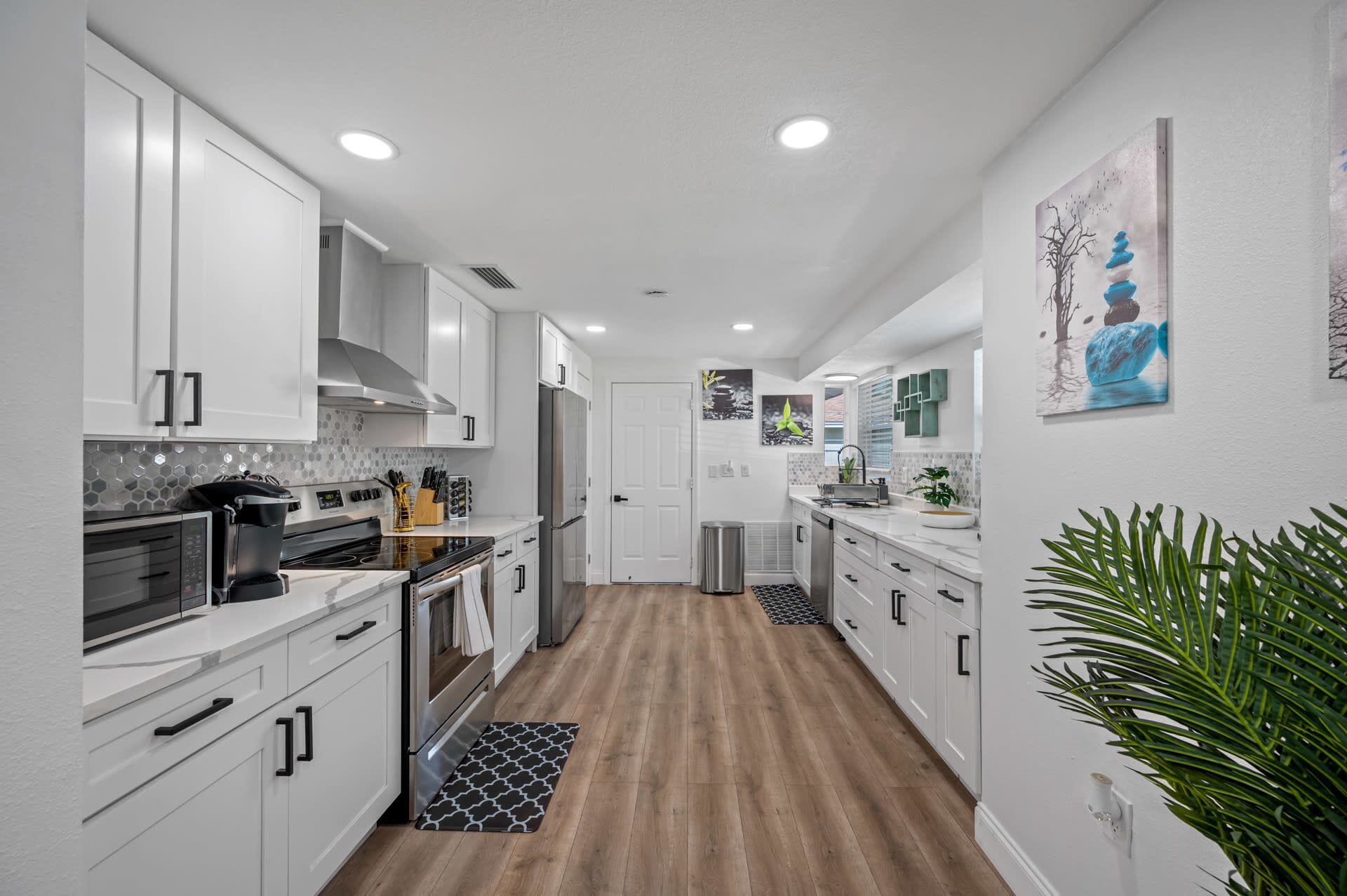 A modern kitchen with white cabinets, stainless steel appliances, and a wooden floor.