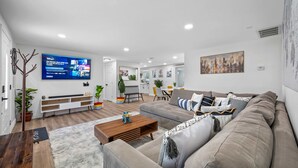Uma sala de estar moderna com um sofá cinza, mesa de centro de madeira e uma TV de tela plana na parede.