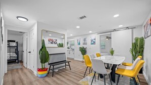 Uma sala de jantar moderna com uma mesa redonda e cadeiras amarelas, um banco preto e uma planta colorida numa cesta vermelha.