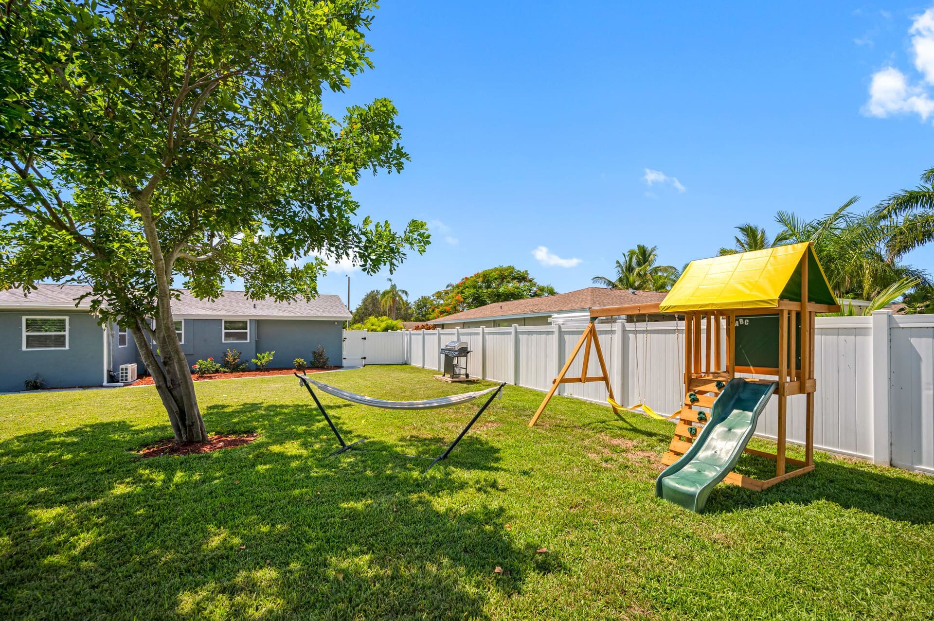 A backyard with a hammock, a swing set, and a slide.