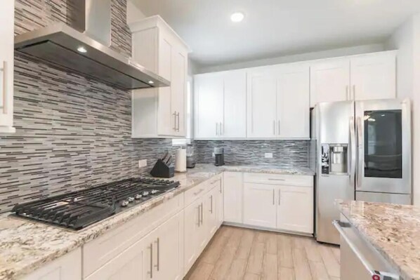 Cocina moderna con armarios blancos, encimera de granito, refrigerador de acero inoxidable y salpicadero decorado.
